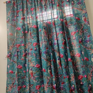 Puede incluir: Cortina de color turquesa con un vibrante estampado floral y de p&aacute;jaros. El dise&ntilde;o presenta flores rojas, p&aacute;jaros y ramas. La cortina cuelga de una barra de madera, a&ntilde;adiendo un toque de elegancia natural a la habitaci&oacute;n.