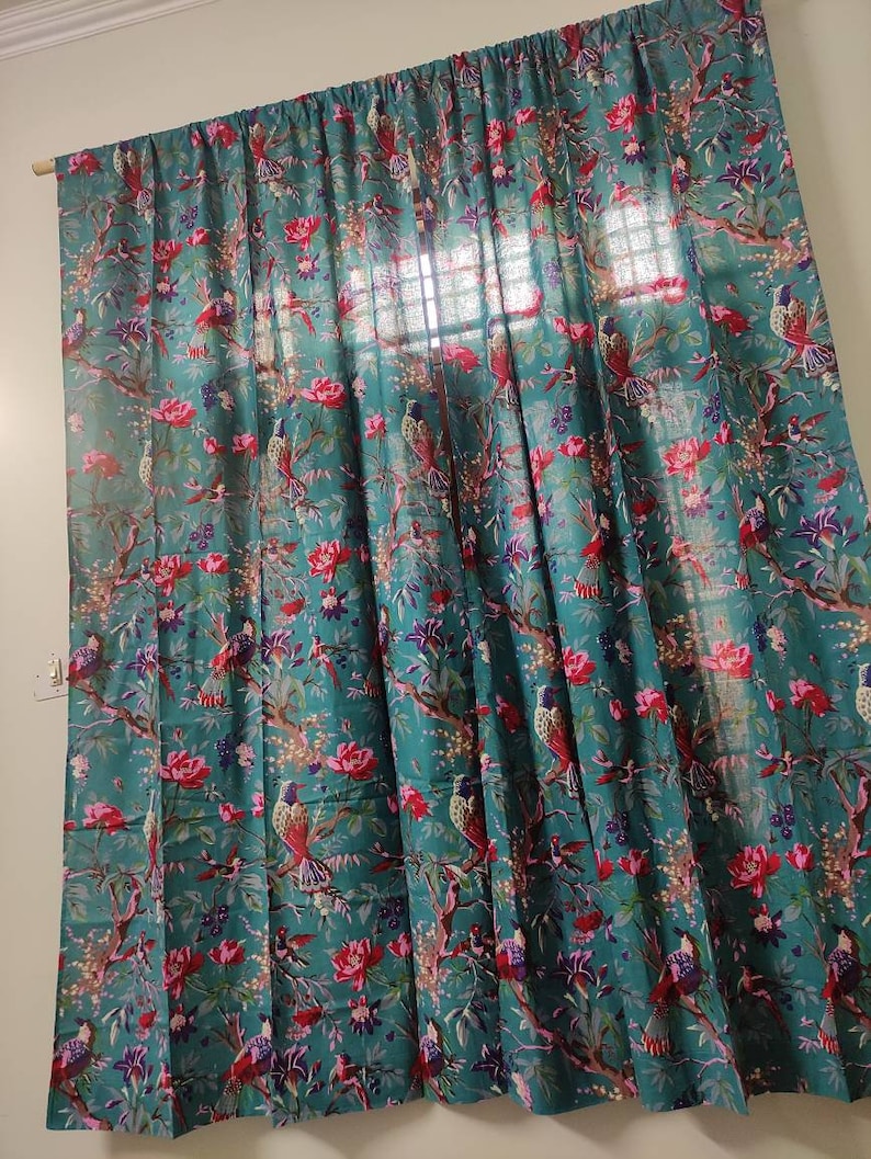 Puede incluir: Cortina de color turquesa con un vibrante estampado floral y de p&aacute;jaros. El dise&ntilde;o presenta flores rojas, p&aacute;jaros y ramas. La cortina cuelga de una barra de madera, a&ntilde;adiendo un toque de elegancia natural a la habitaci&oacute;n.