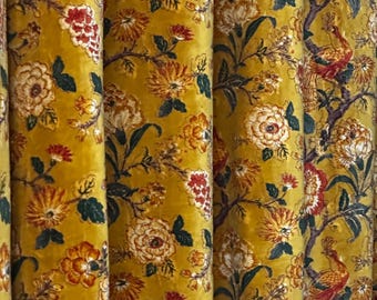 May include: Close-up of a mustard-yellow floral fabric with a velvet texture. The design features large, stylized flowers in shades of cream, orange, and red, along with green leaves. The fabric is likely used for curtains or upholstery.