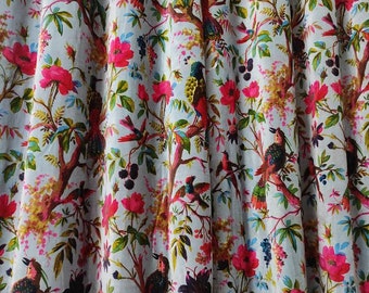 Op de afbeelding: Witte stof met een herhalend patroon van roze bloemen, groene bladeren en kleurrijke vogels. De stof heeft een licht getextureerd oppervlak.