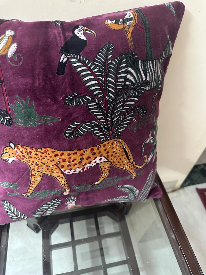 Op de afbeelding: Vierkant kussen in dieppaars. Het heeft een jungle-thema print met een luipaard, toekans en een zebra. Het ontwerp omvat weelderig groen gebladerte op een rijke, fluweelzachte achtergrond.