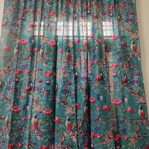 Puede incluir: Cortina de color turquesa con un patr&oacute;n detallado de p&aacute;jaros y flores. El dise&ntilde;o presenta flores rojas y rosas y p&aacute;jaros en las ramas. La cortina cuelga de una barra de madera, a&ntilde;adiendo un toque natural a la habitaci&oacute;n.
