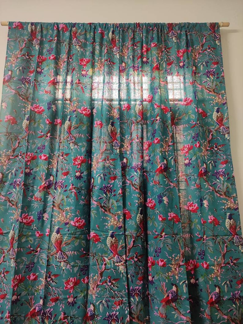 Puede incluir: Cortina de color turquesa con un patr&oacute;n detallado de p&aacute;jaros y flores. El dise&ntilde;o presenta flores rojas y rosas y p&aacute;jaros en las ramas. La cortina cuelga de una barra de madera, a&ntilde;adiendo un toque natural a la habitaci&oacute;n.