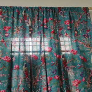 Puede incluir: Cortinas de color turquesa con un vibrante estampado floral y de p&aacute;jaros. El dise&ntilde;o presenta flores rojas, p&aacute;jaros y follaje verde. Las cortinas cuelgan de una barra de madera, a&ntilde;adiendo un toque natural a la habitaci&oacute;n.