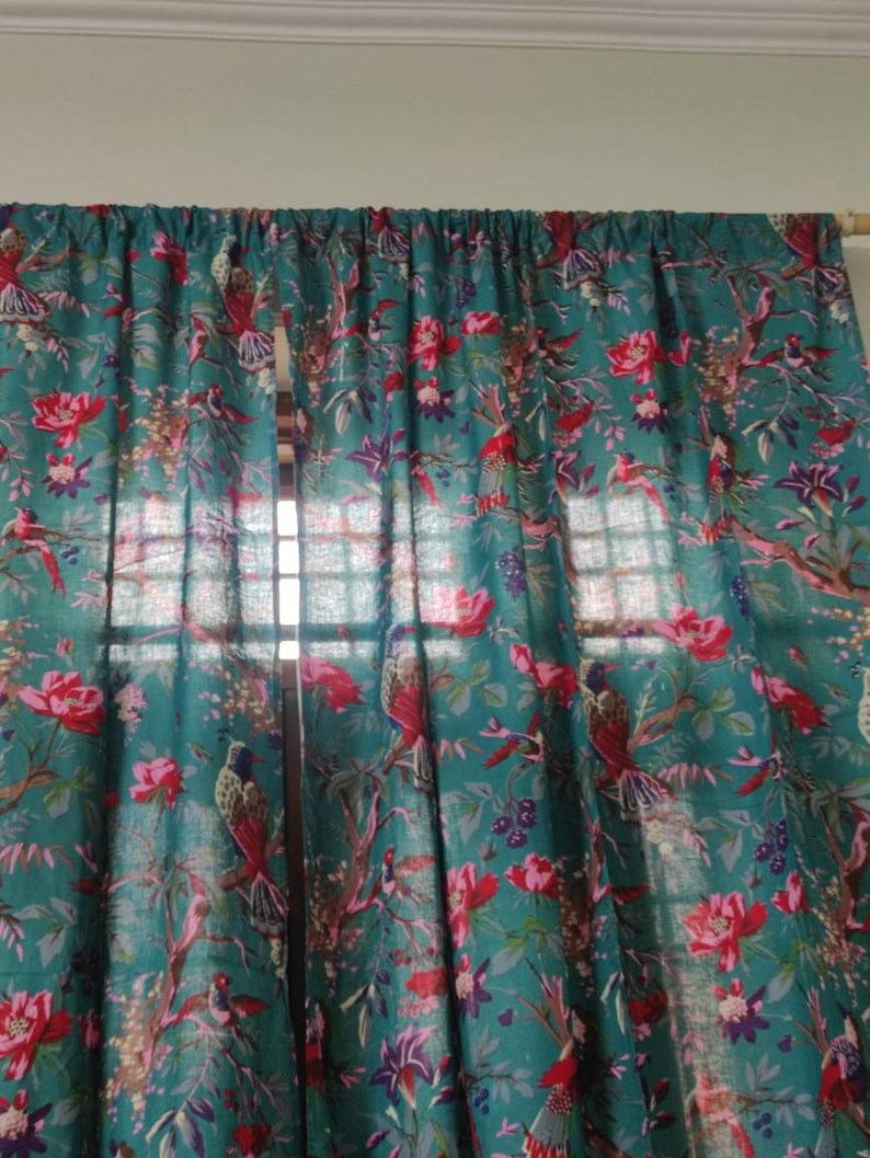Puede incluir: Cortinas de color turquesa con un vibrante estampado floral y de p&aacute;jaros. El dise&ntilde;o presenta flores rojas, p&aacute;jaros y follaje verde. Las cortinas cuelgan de una barra de madera, a&ntilde;adiendo un toque natural a la habitaci&oacute;n.