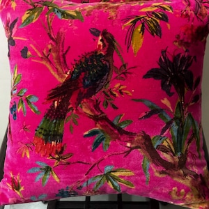May include: A pair of decorative throw pillows with a vibrant pink background. Each pillow features a detailed print of a colorful bird perched on a branch, surrounded by leaves and flowers. The design includes shades of green, blue, and red.