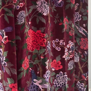 Op de afbeelding: Bordeaux fluwelen gordijnpaneel met een bloemen- en vogelpatroon. Het ontwerp toont rode, paarse en witte bloemen, samen met vogels, tegen een donkere achtergrond. De stof heeft een zachte, luxueuze uitstraling.