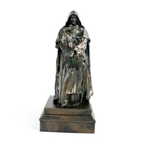 May include: A bronze-colored statue of a robed figure with a hood, holding a book. The statue stands on a rectangular base. The figure's clothing has detailed folds, and the overall style suggests a historical or religious theme.