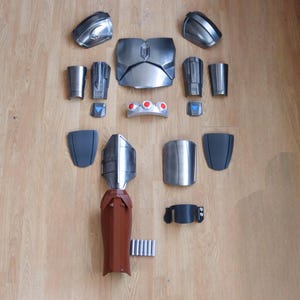 May include: A disassembled silver and brown cosplay armor set, laid out on a wooden surface. The set includes chest and shoulder pieces, arm guards, a belt, and other components. The armor is made of metallic and brown materials.