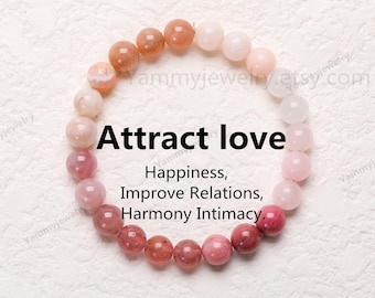 Könnte beinhalten: Ein Armband aus rosa- und pfirsichfarbenen Perlen, kreisförmig angeordnet. Der Text "Attract love" ist zu sehen, zusammen mit Wörtern wie "Glück" und "Harmonie", die ein Thema des Wohlbefindens andeuten.
