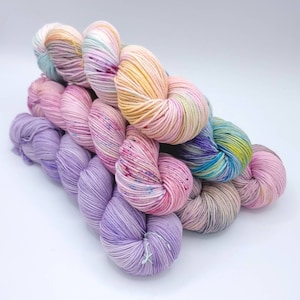 Image of 5 large twisted skeins of yarn stacked upon each other. Skeins are in shades of orange, pink, purple and green.