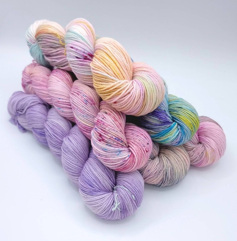 Image of 5 large twisted skeins of yarn stacked upon each other. Skeins are in shades of orange, pink, purple and green.
