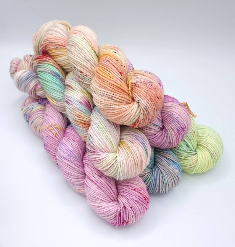 Image of 5 large twisted skeins of yarn stacked upon each other. Skeins are in shades of orange, pink, purple and green.