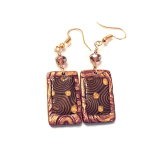 May include: A pair of gold and brown rectangular earrings with a swirl pattern and gold accents. The earrings have a crystal bead on the top of the hook.
