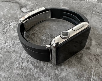 May include: A silver Apple Watch with a black silicone band. The band has a silver buckle.