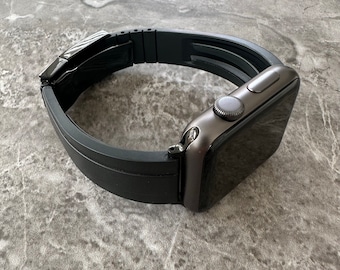 May include: A black smartwatch with a black band. The watch face is dark gray, and the band appears to be made of a flexible material. The watch is displayed on a gray, textured surface.
