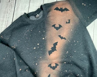 May include: A dark gray sweatshirt with a bleach-splattered design featuring a line of bats on the right side of the garment.