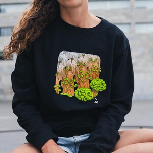 May include: A black sweatshirt with a graphic print of a forest scene. The graphic is in shades of green, brown, and white. The sweatshirt has a crew neck and long sleeves.
