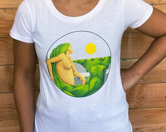 Puede incluir: Camiseta blanca con cuello redondo que presenta un gráfico circular de una mujer con cabello verde y un sol amarillo. La mujer está representada en un paisaje de colinas verdes y cielo azul. La camiseta es de material suave y ligero.
