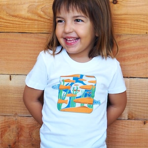 Puede incluir: Camiseta blanca con una ilustraci&oacute;n colorida de peces naranjas nadando en un entorno acu&aacute;tico azul y verde. La camiseta est&aacute; hecha de un material suave y c&oacute;modo, adecuada para ni&ntilde;os.