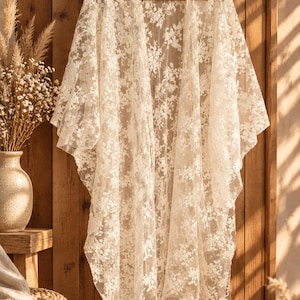 Peut inclure: Un kimono long ouvert sur le devant, confectionné en dentelle transparente de couleur crème avec un motif floral complexe. Le vêtement présente des manches larges et amples ainsi qu'une silhouette fluide et décontractée.