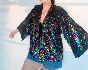 Puede incluir: Un kimono negro de lentejuelas con lentejuelas arcoíris iridiscentes. El kimono tiene cuello en V y mangas largas.