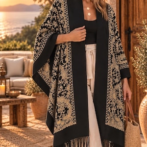 Könnte beinhalten: Ein schwarzer, vorne offener Kimono mit aufwendiger goldfarbener Stickerei in Blumen- und Paisleymustern entlang der Vorderteile und Ärmel. Das Kleidungsstück hat einen einfarbigen schwarzen Kragen und einen Saum mit langen schwarzen Fransen.
