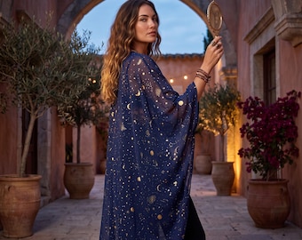 May include: A sheer navy blue kimono featuring a gold celestial print of moons, stars, and planets. The garment has wide, flowing sleeves and an open front design. A small, oval-shaped hand mirror is held up in one hand, reflecting light.