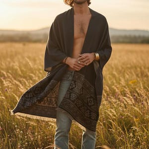 Könnte beinhalten: Ein dunkelgrauer Kimono-Wrap mit gemustertem Saum, kombiniert mit blauen Jeans. Der Wrap ist über den Schultern drapiert und gibt die Brust frei. Der Hintergrund ist ein Feld mit hohem Gras unter einem warmen Sonnenuntergang.
