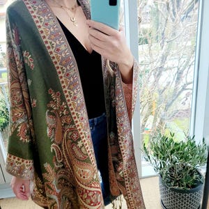 Peut inclure: Un châle à motifs paisley vert et marron avec une bordure frangée. Le châle est drapé sur les épaules d'une personne et porté avec un haut noir et un jean bleu.