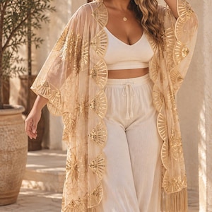 May include: A sheer beige kimono featuring gold sequin fan-shaped patterns along the front edges and hem. The garment has an open front, wide three-quarter length sleeves, and a long fringe trim along the bottom edge, creating a layered look.