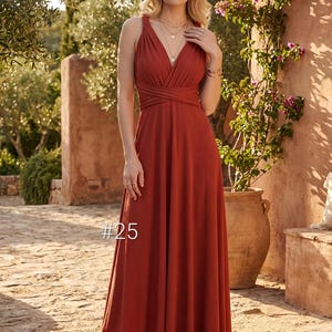 Könnte beinhalten: Ein rostfarbenes Maxikleid mit V-Ausschnitt und gekreuztem Oberteil. Das Kleid hat einen fließenden Rock und wird im Freien getragen. Die Nummer "#25" ist auf dem Kleid zu sehen. Das Model trägt goldene Halsketten und Armbänder.