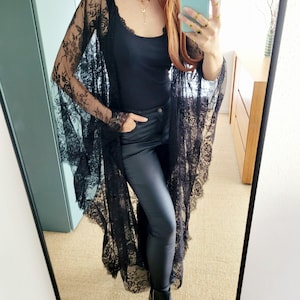 Peut inclure: Un kimono en dentelle noire avec des manches longues et un ourlet festonné. Le kimono est porté sur un débardeur noir et un pantalon noir en similicuir. La tenue est complétée par des bottines noires.