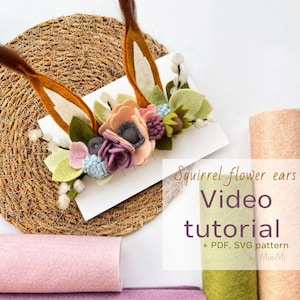 Può includere: Fascia per capelli in feltro con orecchie di fiori di scoiattolo, con tutorial video, modello PDF e SVG. La fascia è decorata con fiori in feltro in tonalità di rosa, viola, verde e blu. La fascia è su uno sfondo bianco con un tappetino intrecciato e quadrati di feltro rosa, verde e pesca.