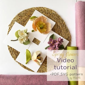 May include: Four felt flower arrangements on white cards, including a pink poppy, white jasmine, pink lilac, and a white flower with green leaves. The cards are on a woven straw mat. The text "Spring flowers Video tutorial +PDF, SVG pattern by MiniMi" is below the flowers.