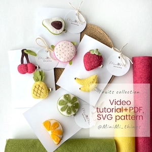 May include: A set of felt fruit hair clips, including a pineapple, strawberry, avocado, cherry, lime, banana, and orange. The clips are displayed on white cards with the text "Fruits collection Video tutorial+PDF, SVG pattern @MiniMi-things".