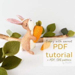Könnte beinhalten: Ein Filzhase hält eine Filzkarotte. Der Hase ist braun mit rosa Ohren und einem weißen Gesicht. Die Karotte ist orange. Das Bild enthält den Text "Bunny with carrot PDF tutorial + PDF, SVG pattern by MiniMi".