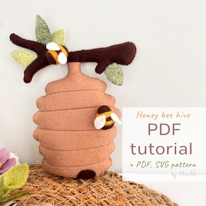 May include: A felt honey bee hive with a branch and leaves, two bees, and the text "Honey bee hive PDF tutorial + PDF, SVG pattern by MiniMi".