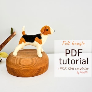 Pode incluir: Tutorial PDF de beagle de feltro com modelos PDF e SVG da MiniMi. A imagem mostra um beagle de feltro marrom, preto e branco em pé sobre uma base de madeira.