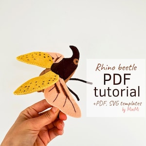 Op de afbeelding: Een vilten neushoornkever knutselproject met een PDF-tutorial en SVG-sjablonen. De kever is bruin, geel en roze met zwarte ogen. De tekst op de afbeelding luidt "Rhino beetle PDF tutorial +PDF, SVG templates by MiniMi".