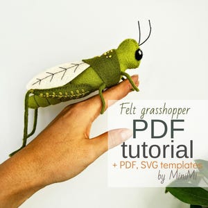 May include: A handmade felt grasshopper in shades of green, with white and black accents. The grasshopper has detailed wings and is perched on a hand. The image includes the text "Felt grasshopper PDF tutorial + PDF, SVG templates by MiniMi".