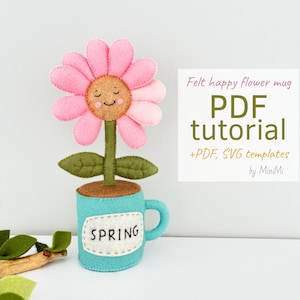 May include: Felt flower mug craft tutorial with PDF and SVG templates. A pink flower with a smiling face is in a blue mug with the word "SPRING" on it.