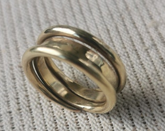 May include: A gold ring with three bands that are intertwined. The ring is made of a smooth, shiny metal.