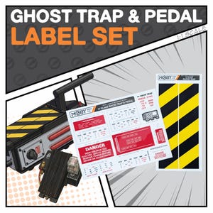 May include: A Ghost Trap & Pedal Label Set with a 1:1 scale. The set includes labels with warnings and danger notices, along with a black and yellow striped design. The image also shows a black and silver prop with a handle.