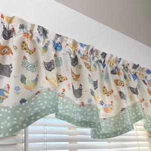 May include: A valance curtain with a cream background and a repeating pattern of colorful chickens. The bottom edge features a light green fabric with white polka dots. The curtain is mounted above a window.