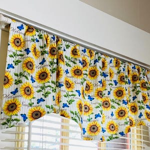 K&ouml;nnte beinhalten: Ein Gardinenvolant mit wei&szlig;em Hintergrund, vertikalen Streifen und einem sich wiederholenden Muster aus Sonnenblumen und blauen Schmetterlingen. Das Wort "Sunflower" ist auf dem Vorhang geschrieben.
