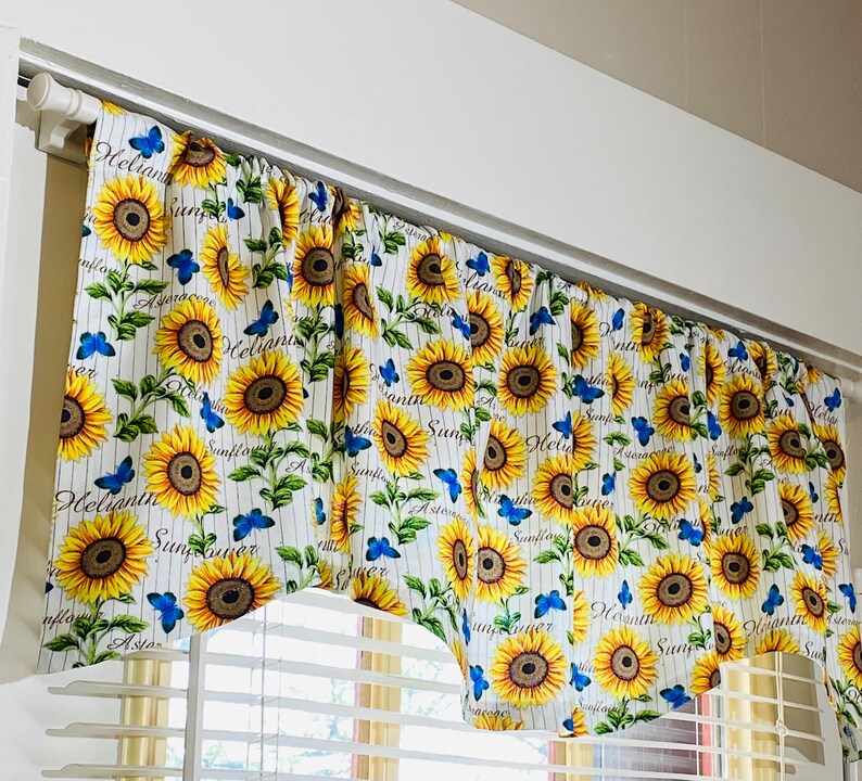 K&ouml;nnte beinhalten: Ein Gardinenvolant mit wei&szlig;em Hintergrund, vertikalen Streifen und einem sich wiederholenden Muster aus Sonnenblumen und blauen Schmetterlingen. Das Wort "Sunflower" ist auf dem Vorhang geschrieben.