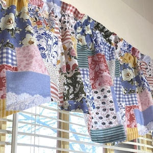 May include: A patchwork valance with a variety of floral, gingham, and striped patterns in shades of blue, pink, red, yellow, and white. The valance is hanging above a window with white blinds.
