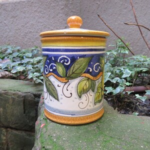 May include: A ceramic jar with a yellow, blue, and white floral design. The jar has a lid with a knob on top.
