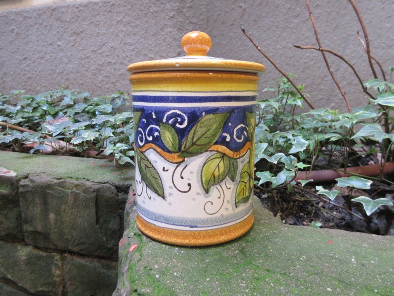 May include: A ceramic jar with a yellow, blue, and white floral design. The jar has a lid with a knob on top.